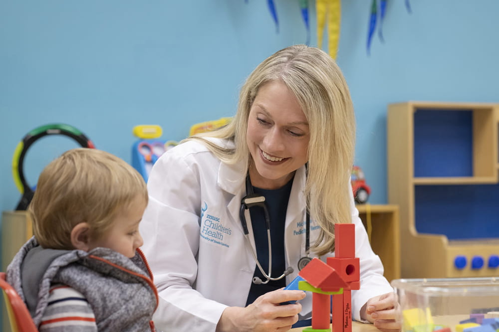 a female doctor sits at a low table with a child in a playroom