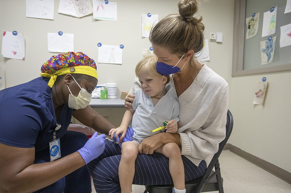 A woman gives a little boy a vaccine as his mother holds him