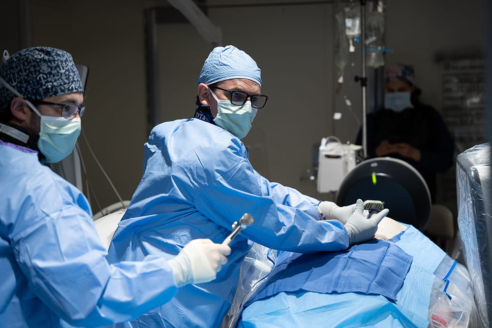 a doctor in surgical gear works on a patient while looking at a screen