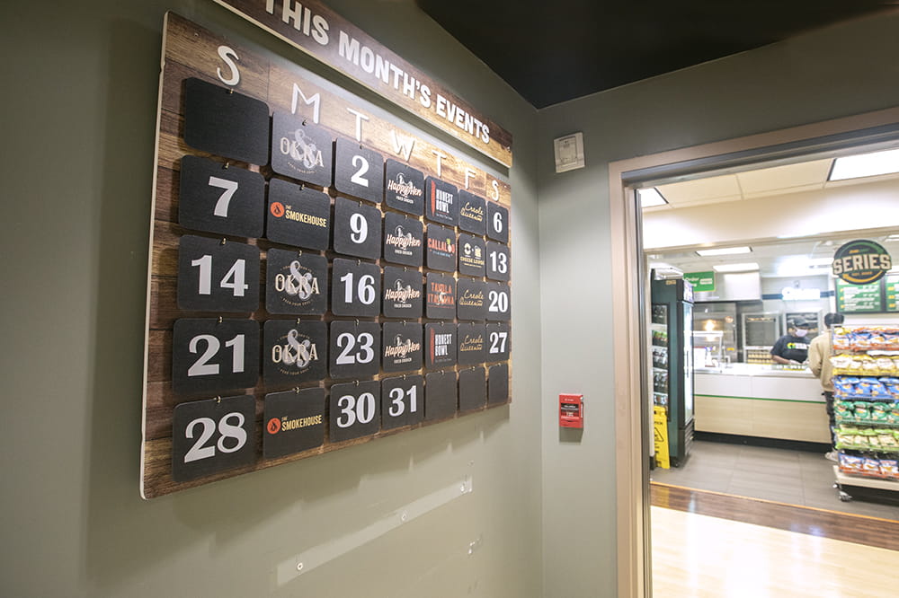 A wall calendar with removable dates and tiles that list different menu options. It is hanging in the cafeteria by the entrance.
