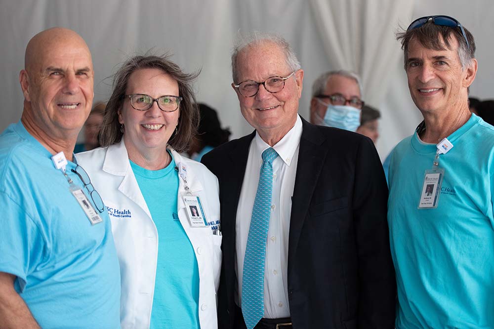 Four people stand together smiling at the camera.  There is a woman and three men.  They are dressed in medical clothing.  LR Steve Shugart, Director of Chaplaincy, Tallulah Holmstrom, CMO Midland's Division;  Dr Mac Leppard, Andrew W., Chaplain  