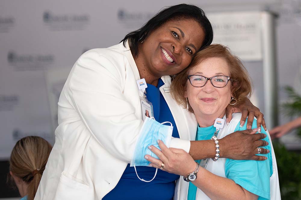 A tall woman hugs a shorter one. The tall woman is Susan Burroughs, associate chief executive officer, MUSC Health Columbia Medical Center Northeast. The other woman is Pam Roberts, lab director at MUSC Health Kershaw Medical Center.