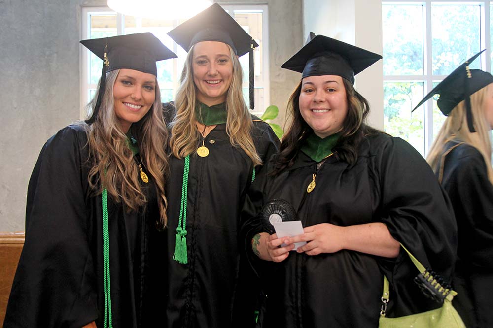Three women in graduation regalia stand together smiling.