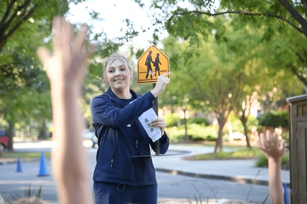 A female physican holds up a miniature street sign for elementary school students