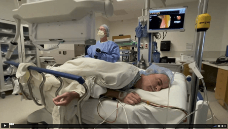 A still image of a man on the operating room table, getting a colonoscopy