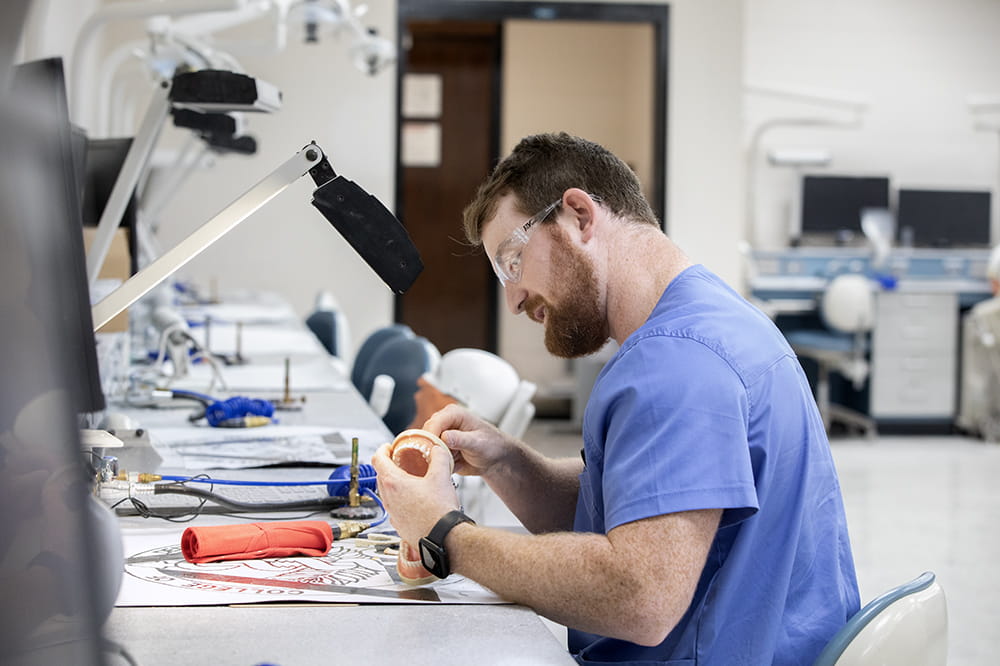 A young man with a beard, works on a set of cast teeth in MUSC's dental simulation lab