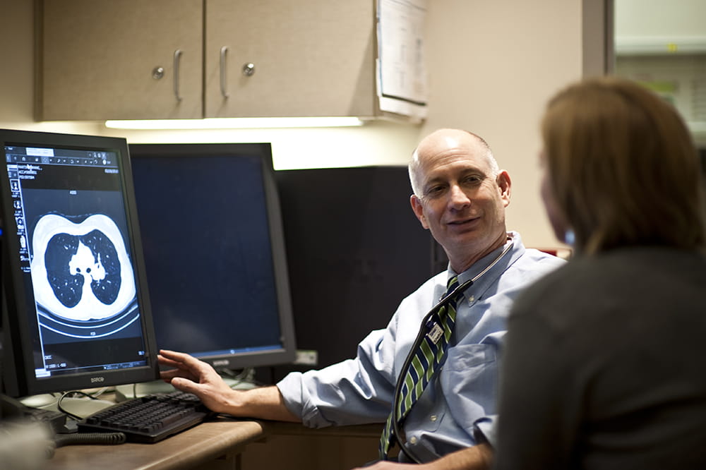 a man at a desk gestures at a lung scan on a screen