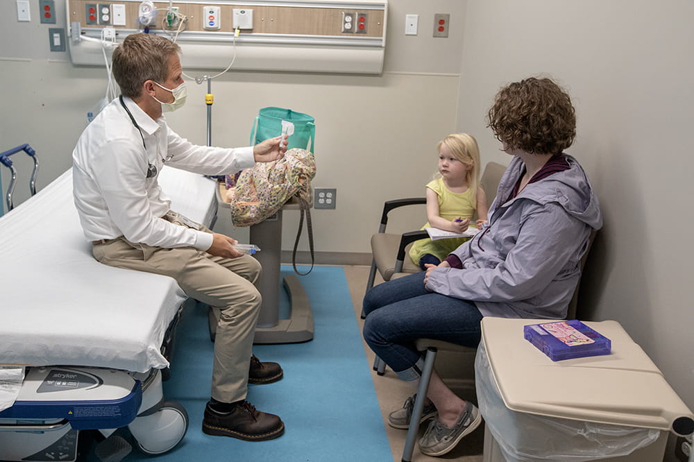 Girl looks skeptically at doctor who is holding a vial for her to spit into.