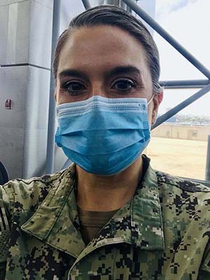 Headshot of a woman veteran wearing a blue surgical mask and camouflage jacket. Her brown hair is pulled back from her face.
