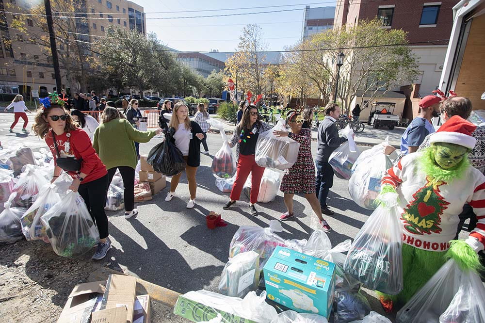 MUSC employees pick up bags filled with gifts for children at the Angel Tree Parade. One is dressed as the Grinch. Others are wearing festive sweaters and hats.