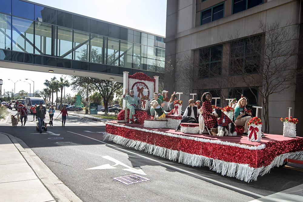 People on a red and white float wave to people standing along the Angel Tree Parade route.