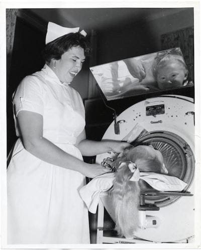 A nurse shares a smile with a child inside an iron lung.   City of Boston Archives from West Roxbury, United States, CC BY 2.0, via Wikimedia Commons
