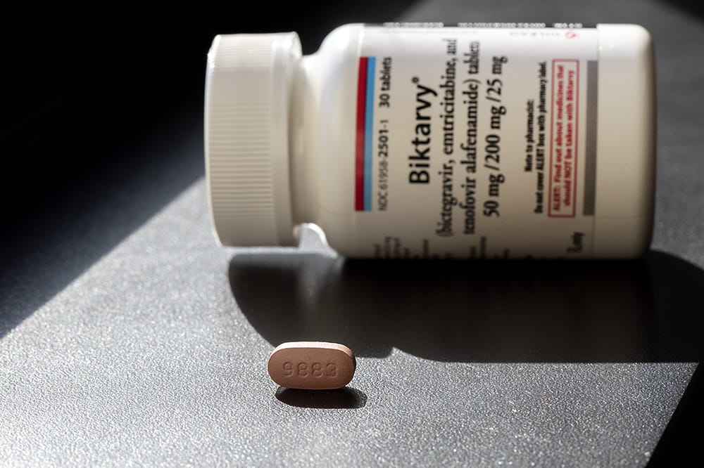 Pill bottle labeled Biktarvy lying on its side with a single brown pill in front of it.