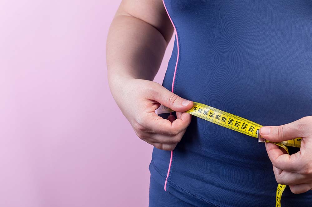 Overweight woman with measuring tape around her waist.