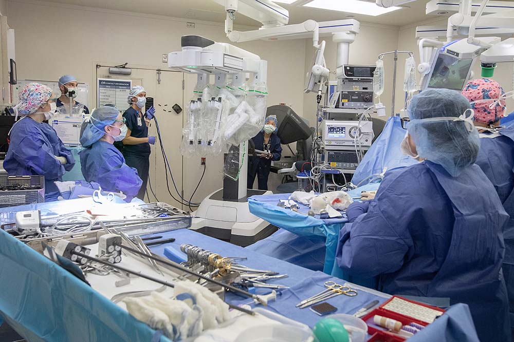 Several people in scrubs with hair covered work in an operating room.