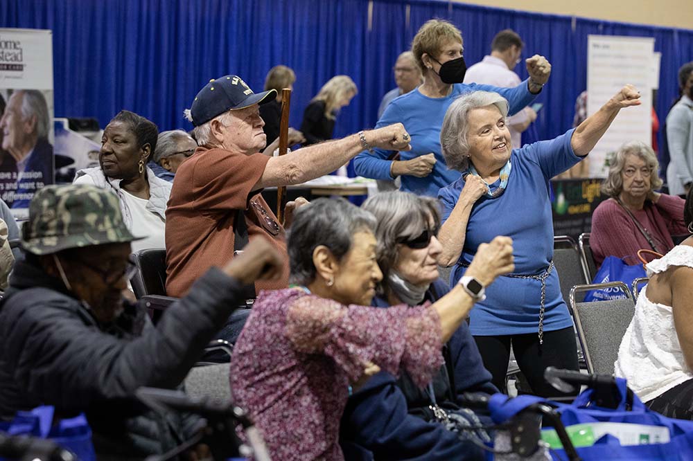 People making punching motions at Senior Expo. A petite woman is the focus of the photo.