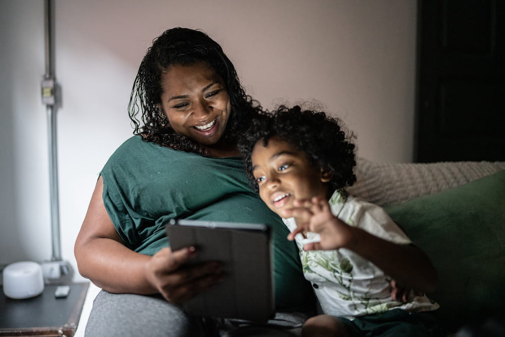 A woman and child look at an iPad while sitting on a couch
