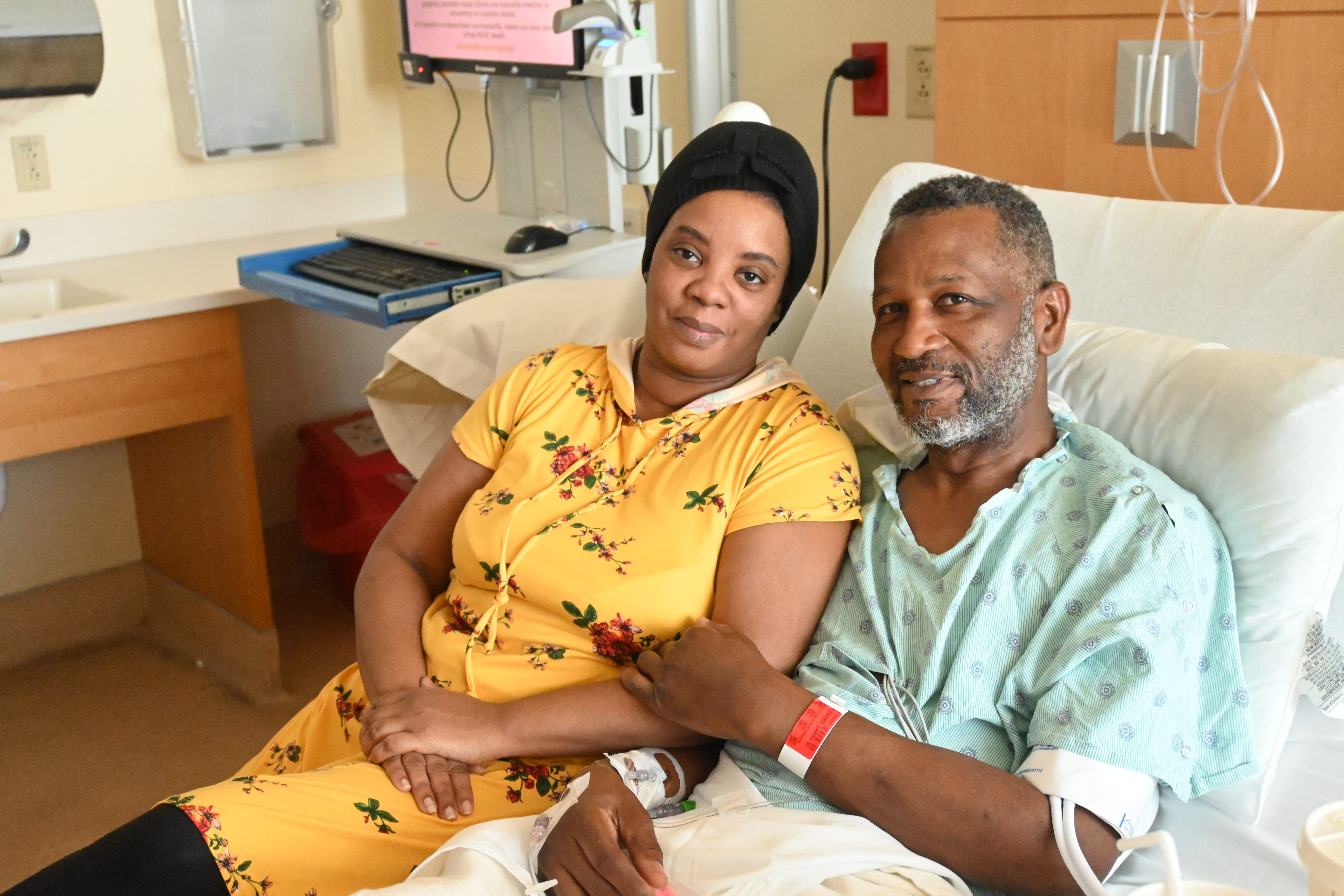 A woman and man smile in a hospital bed. The man is the patient. She is visiting him.