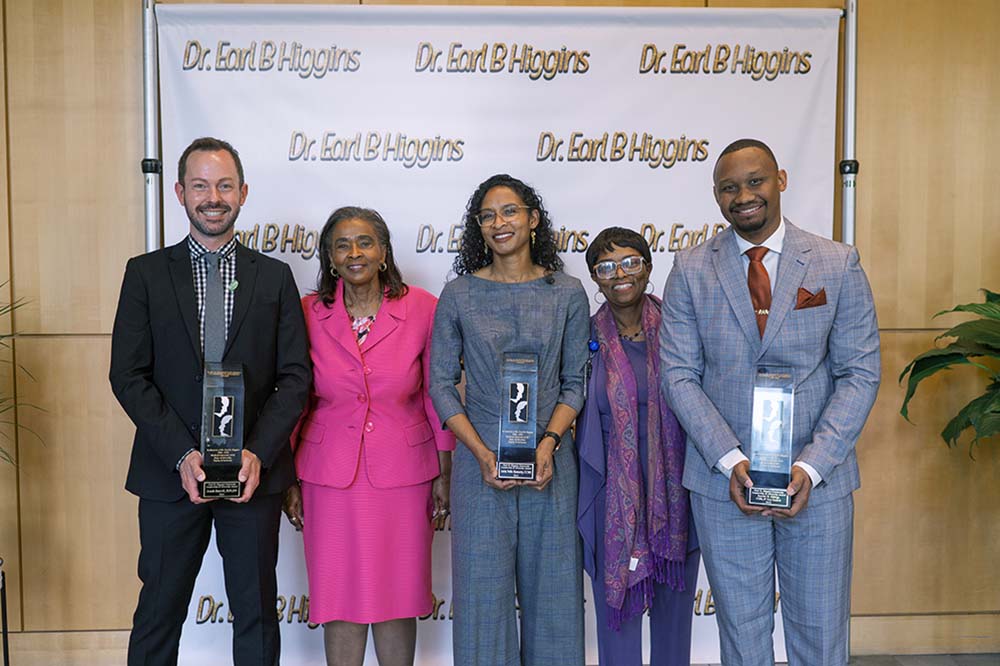 Three women and two men smile while holding awards.