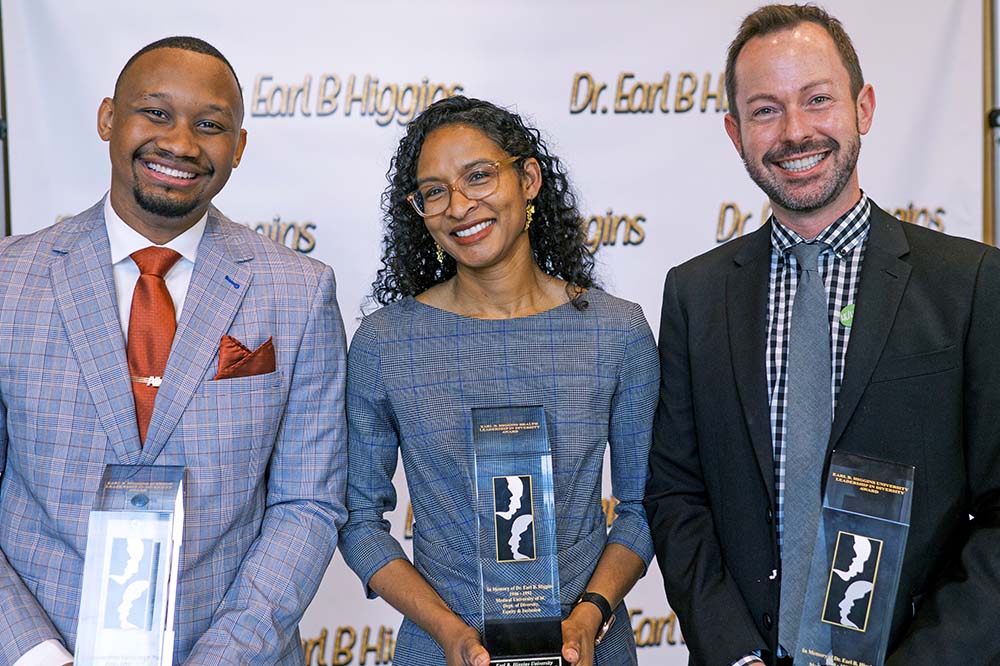 Two men and a woman smile while holding awards against a background that says Dr. Earl B. Higgins.