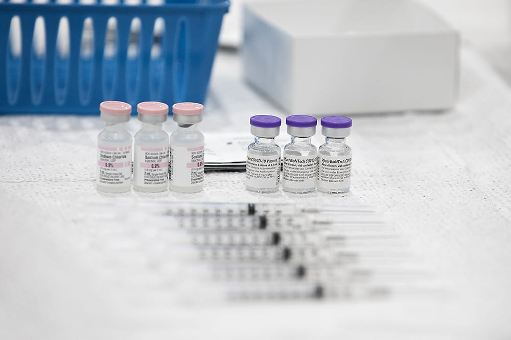 Syringes lying in front of vials of COVID-19 vaccine. 