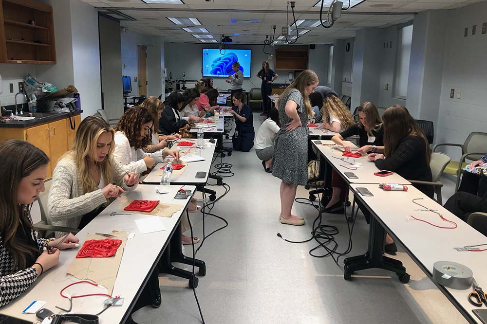 Two tables facing each other with young women seated behind them working on suturing.