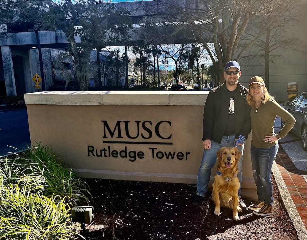 A man, a woman and a dog stand in front of a sign that says Rutledge Tower