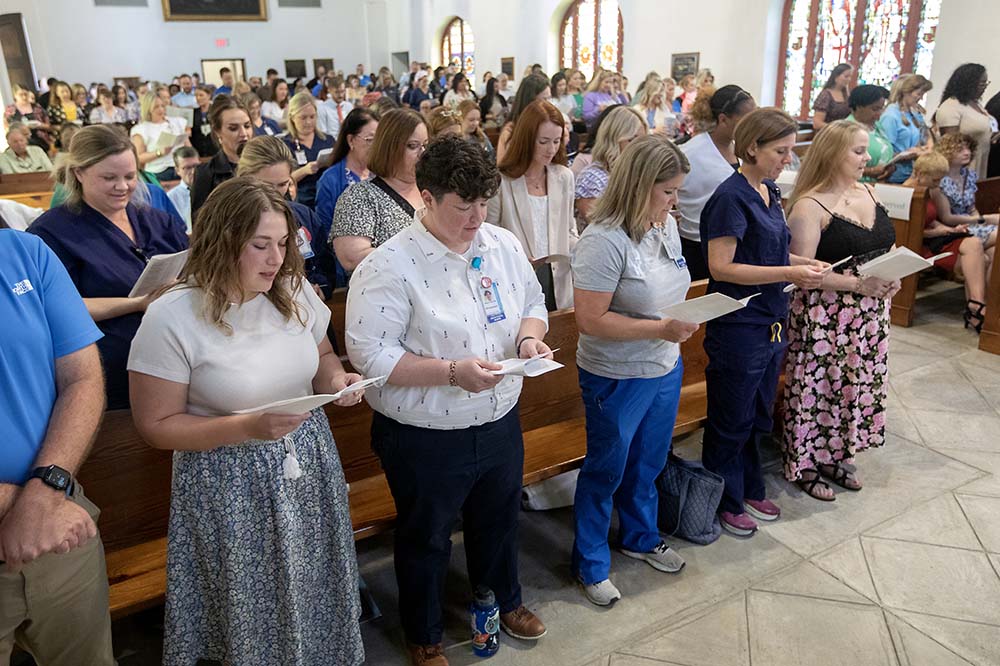 People in church pews stand to read from papers in their hands.