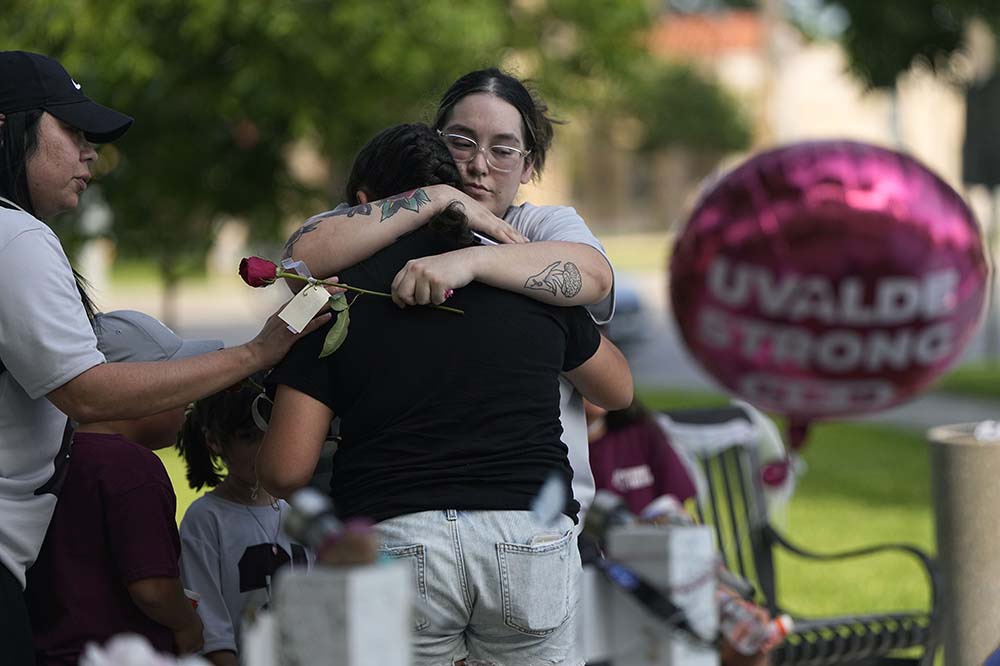A woman hugs someone whose back is to the camera. A pink balloon floats beside them with the words Uvalde Strong on it.