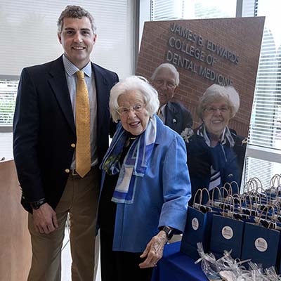 A tall young man in a costume and tie stands with an older woman who is wearing blue and smiling.
