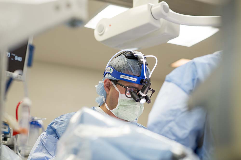 A surgeon wearing a mask and surgical goggles. You can't see the patient he's working on.