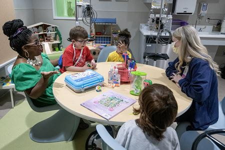 Five people, two adults and two children sit around a table in a hospital playroom