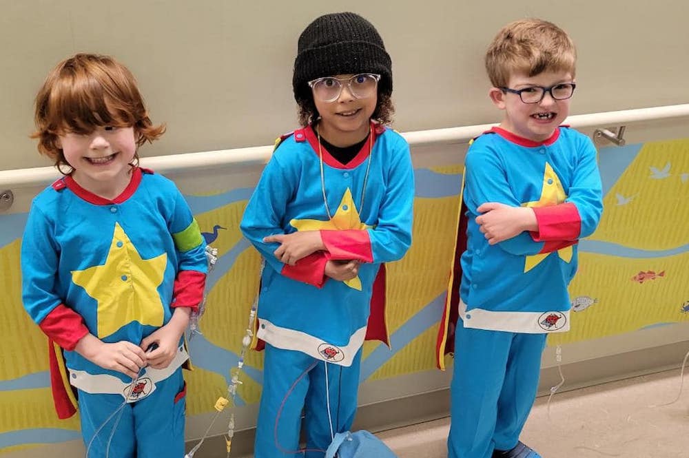 All three boys wearing blue superhero costumes, with yellow stars on front and a red cape.