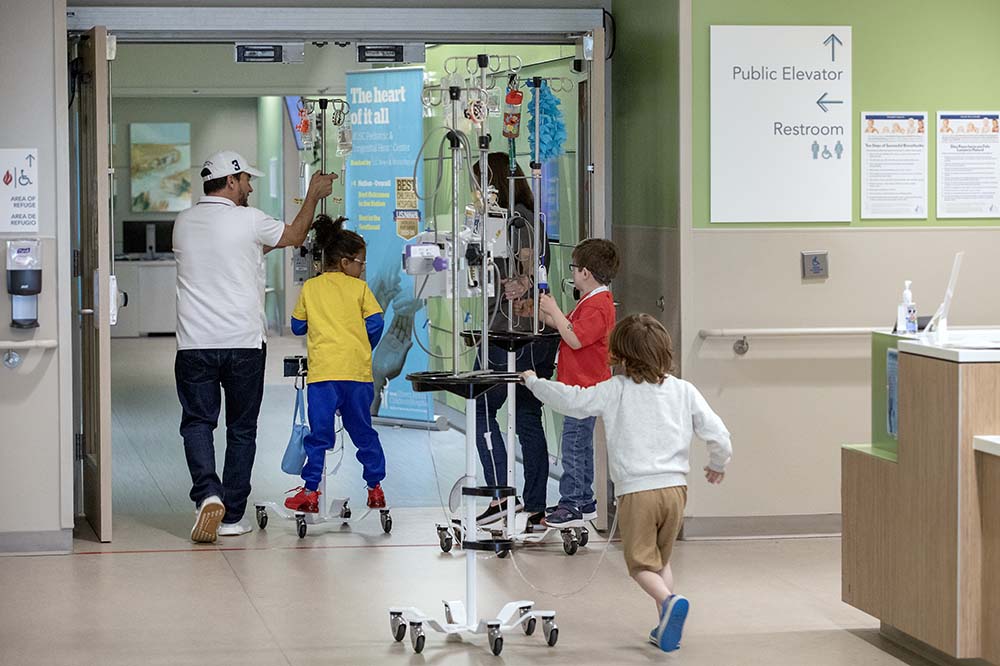 Boys ride IV stands through a hospital hallway.
