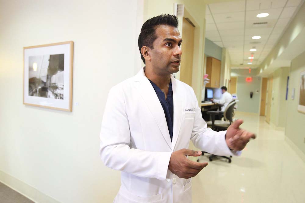 Doctor in a white jacket gestures while speaking in a hallway.