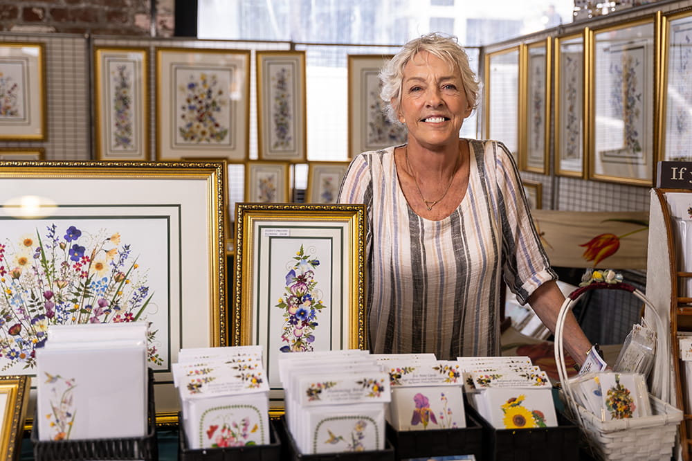 a woman stands in her booth surrounded by her art 