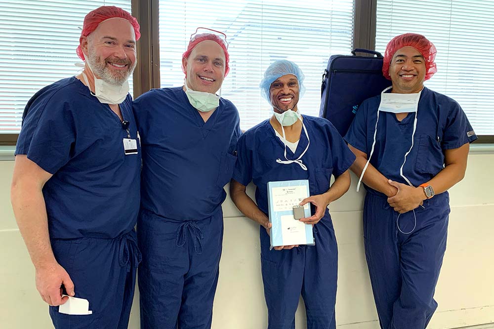 Four men wearing blue scrubs smile while standing together.