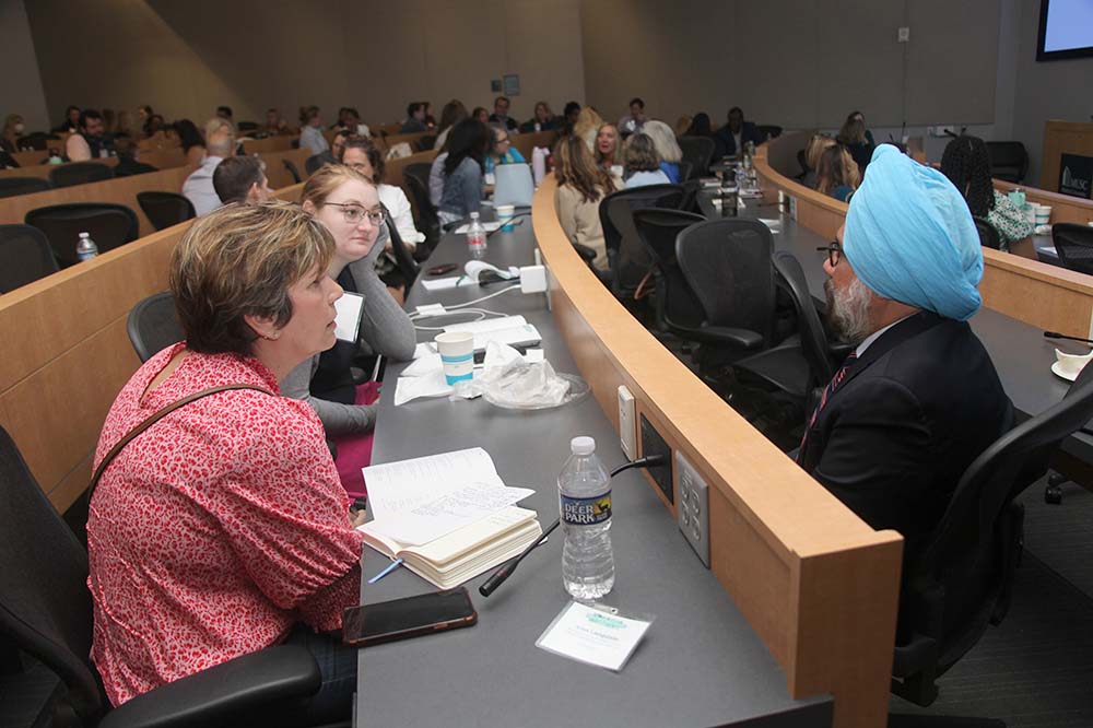 People face each other during a discussion. Two are women. One is a man wearing a blue turban and a suit.