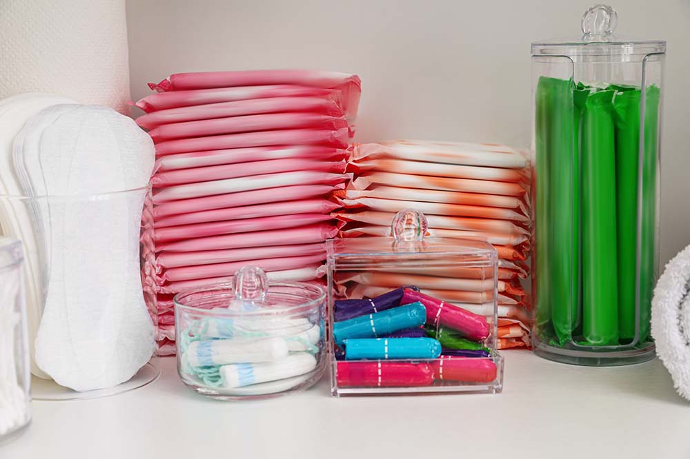 White sanitary pads, stack of pink pads, stack of orange pads, jar of tampons wrapped in green.
