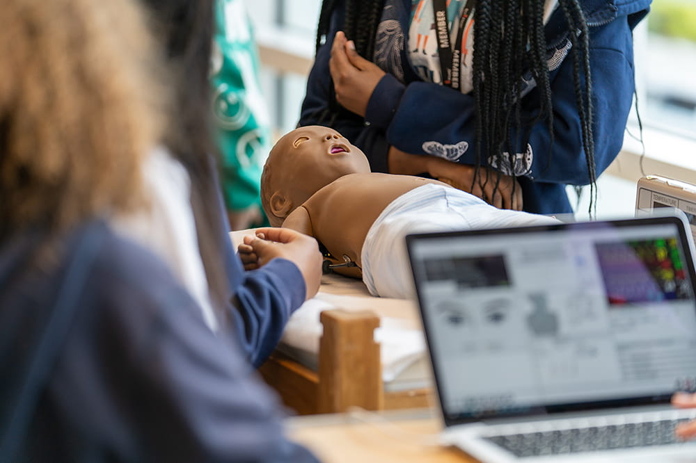 a group of students gather around a medical manikin of an infant