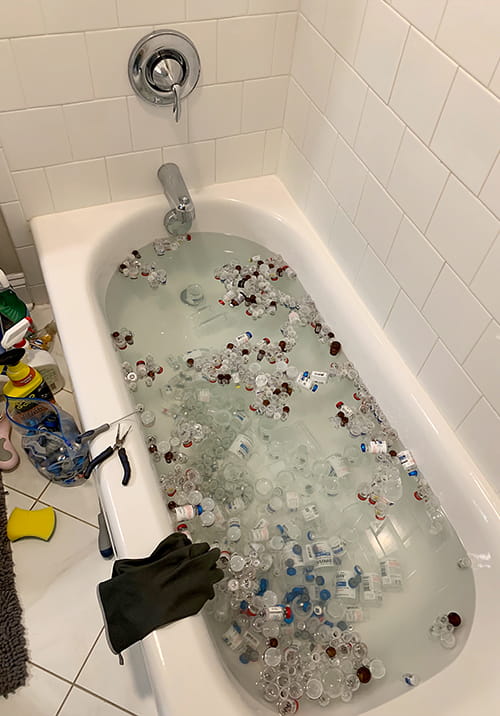 Bathtub filled with glass medical vials and water.