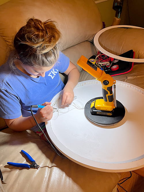 Woman in blue tshirt with her hair up uses soldering equipment.