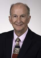 Man smiling for portrait. He's wearing a pink shirt, a necktie and a suit jacket.