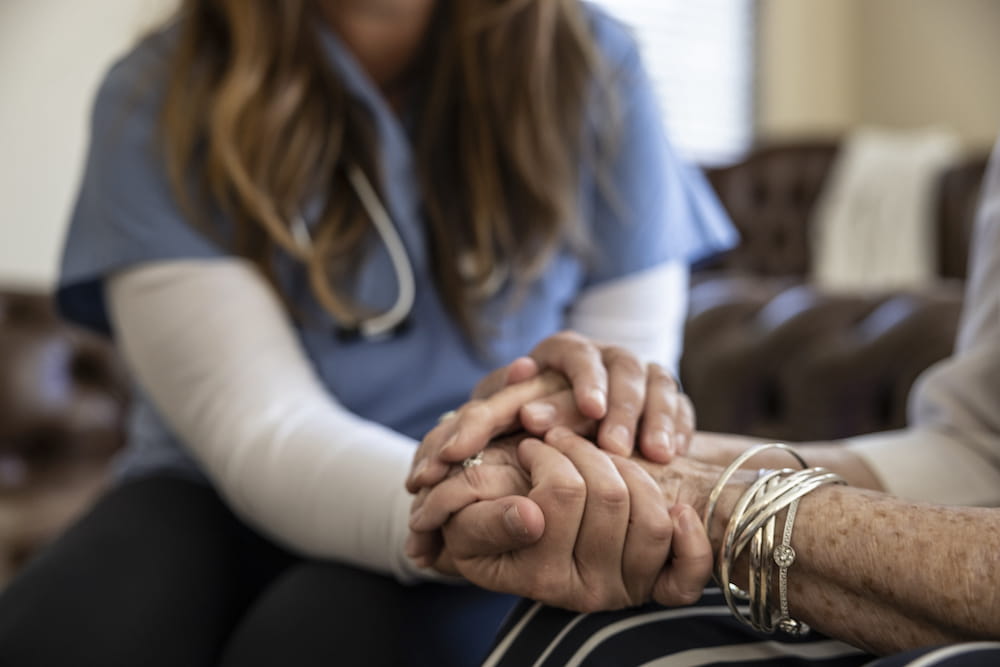 A close up of a health care worked holding the hands of an older patient. 