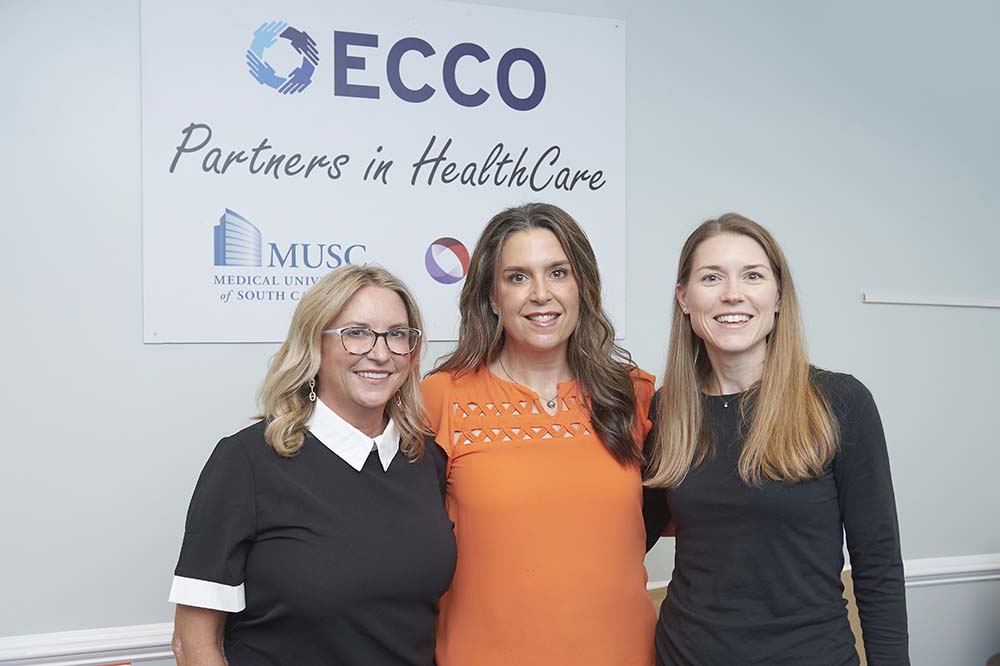 Three women stand in front of poster that says ECCO. Partners in health care.