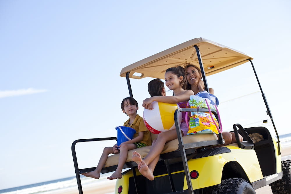 A family rides in a golf cart on the beach