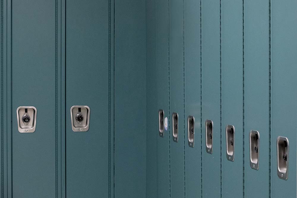 Series of blue lockers with silver locks. The picture focuses on the turn between two lines, which sit in an L shape.