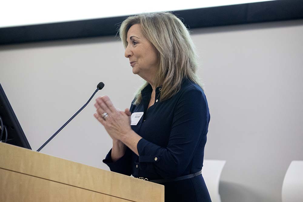 Blonde woman wearing a dark suit holds her hands in prayer position while speaking at a podium.