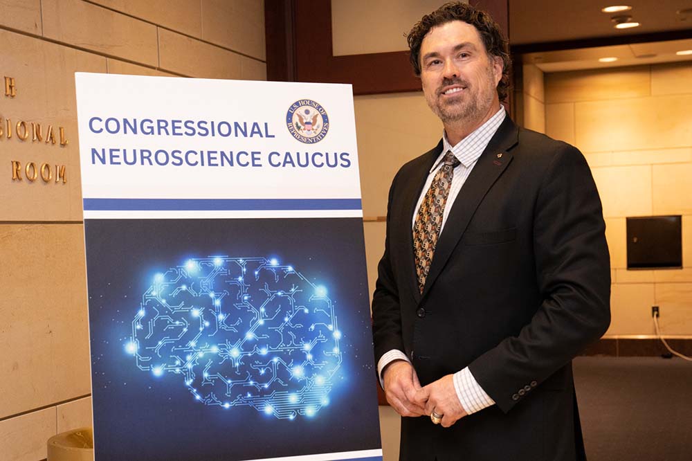 Man in a suit stands beside a poster that Congressional Neuroscience Caucus.