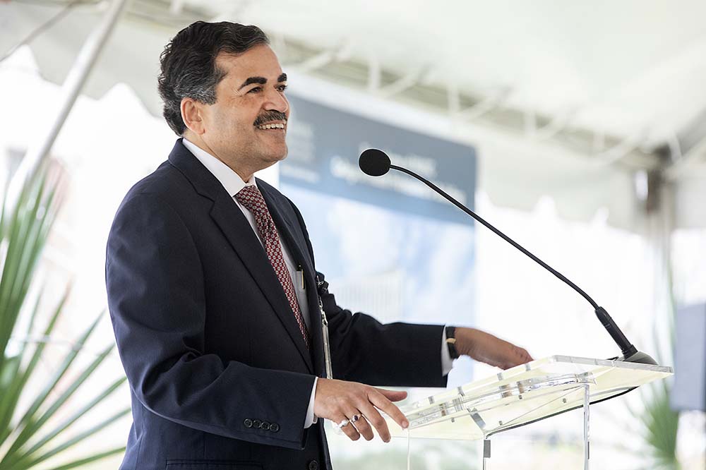 Smiling man with a mustache wearing a suit and tie speaks at a podium.